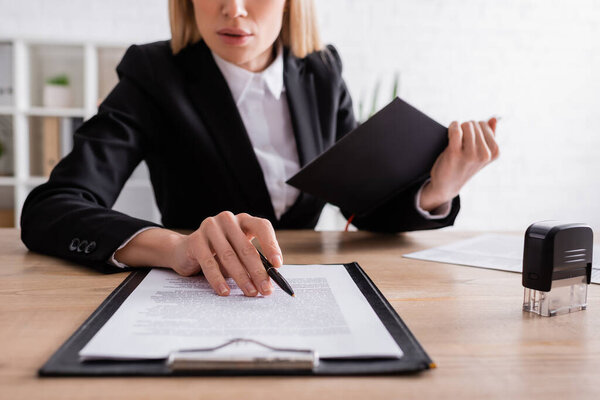 partial view of notary with notebook holding pen near clipboard with contract