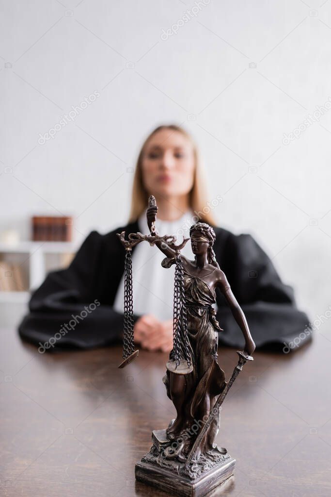 selective focus of themis statue near prosecutor in black mantle sitting on blurred background