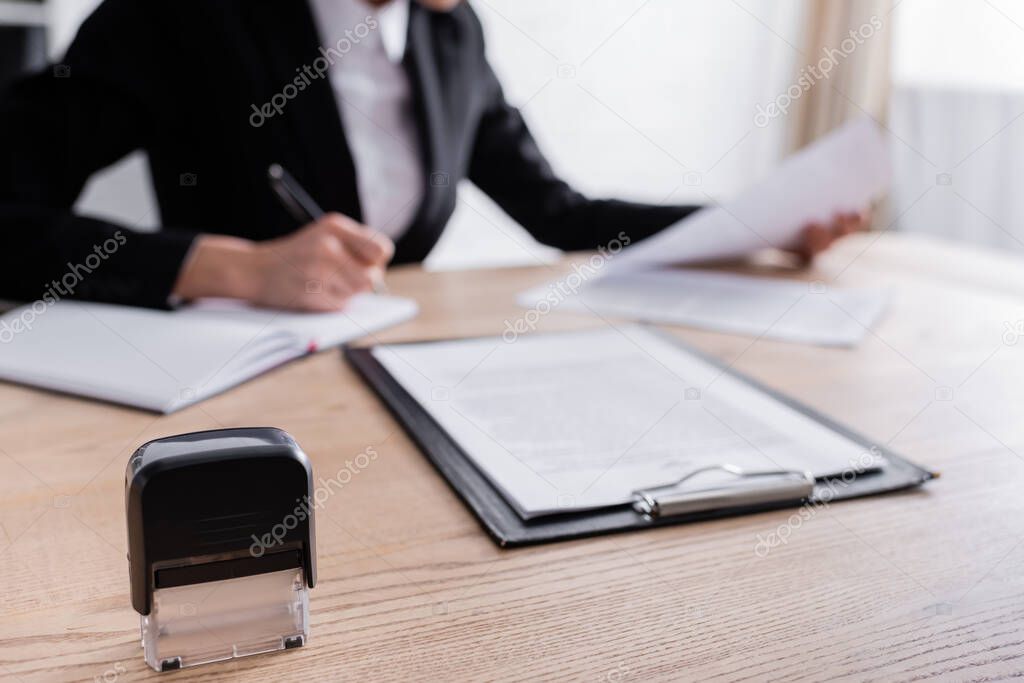 selective focus of stamper and clipboard near cropped notary writing on blurred background