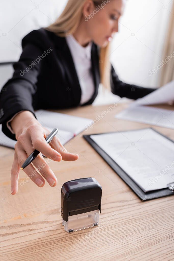 lawyer reaching stamper while working with documents on blurred background