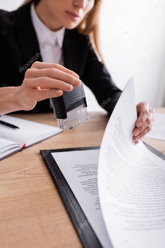 partial view of lawyer holding stamper near contract on blurred background