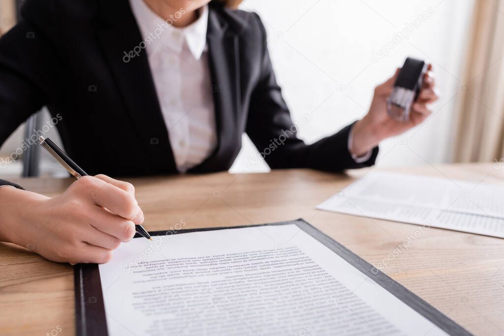 partial view of notary signing contract and holding stamper on blurred background