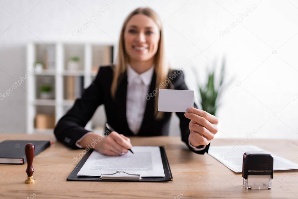 happy notary holding blank business card while sitting on blurred background