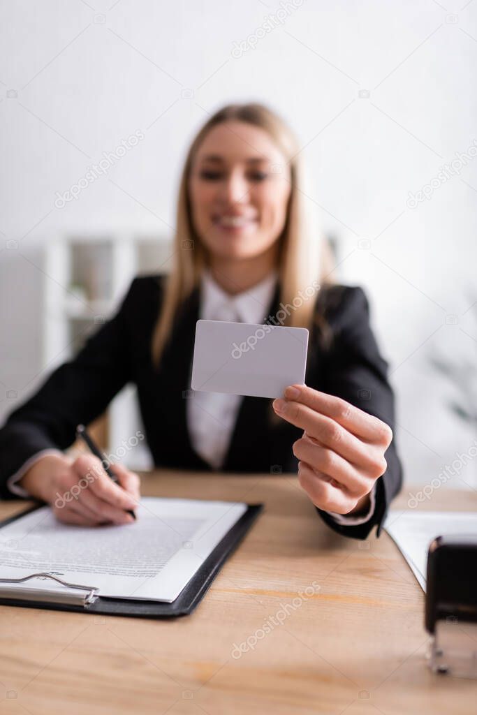 smiling notary holding blank business card on blurred background