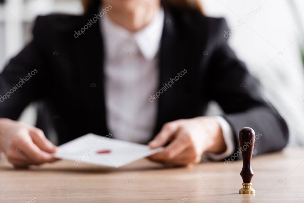 selective focus of stamper near cropped notary with envelope on blurred background