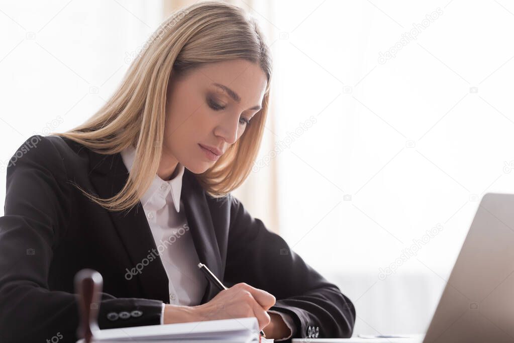 blonde notary in formal wear writing in office