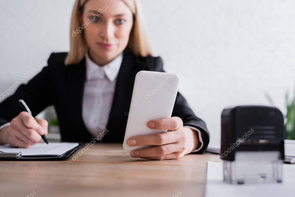 notary holding smartphone near stamper on blurred foreground