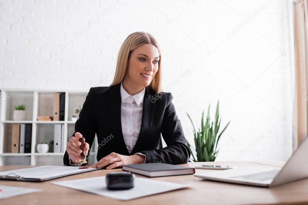 smiling notary looking at laptop while stamping contract in office