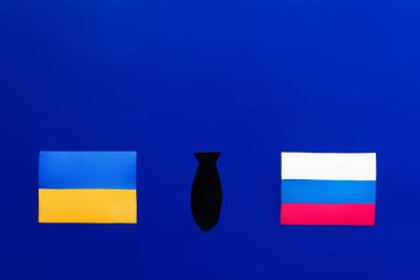 Mavi arka planda Ukrayna ve Rusya bayrakları arasındaki kağıt bombasının en üst görüntüsü 