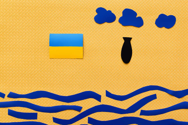 Вид сверху на украинский флаг и бумажную бомбу над картонным морем на текстурированном желтом фоне 