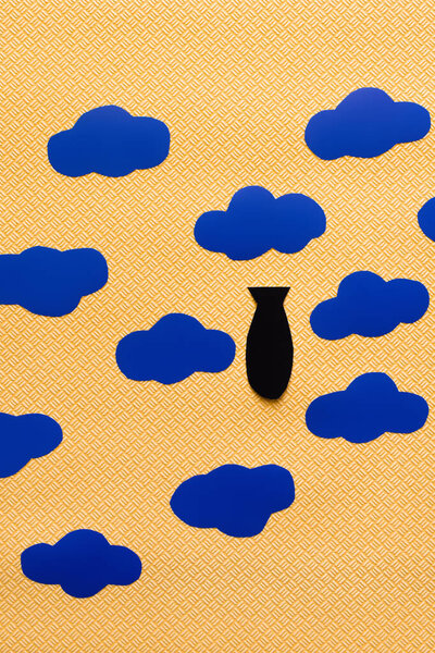 Вид сверху на бумажную бомбу и картонные облака на текстурированном желтом фоне, война в концептуальном виде 