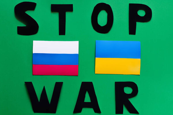 Top view of stop war lettering and ukrainian and russian flags on green background 
