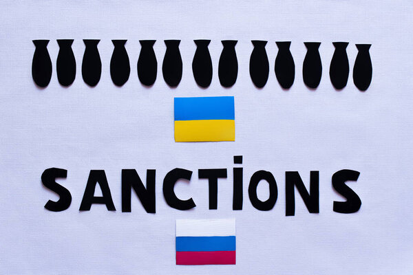Top view of paper bombs, sanctions lettering near ukrainian and russian flags on white background 