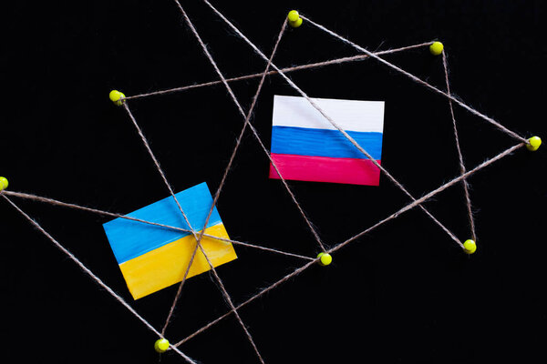 Top view of push pins with thread, ukrainian and russian flags isolated on black 