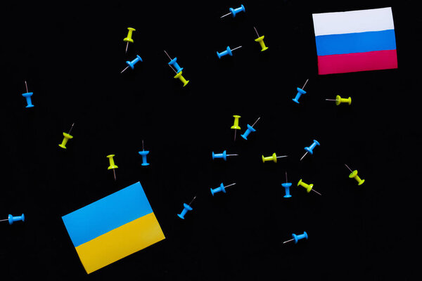 Top view of ukrainian and russian flags near push pins isolated on black 