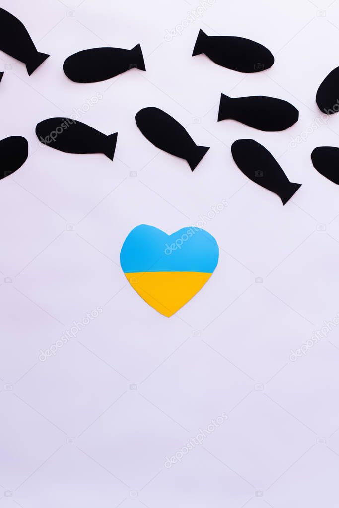 Top view of ukrainian flag in heart shape under paper bombs on white background 