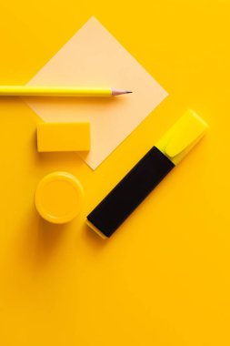 Silginin, kalemin, kavanozun, boyanın ve keçeli kalemin üst görüntüsü sarı kağıdın yanında.
