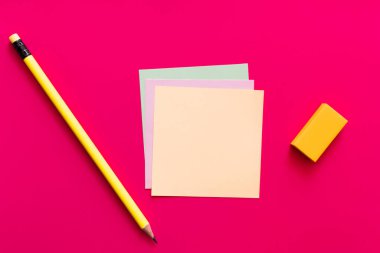 Pembe arkaplan üzerine çok renkli kağıt notların yanındaki kalem ve silginin üst görünümü 