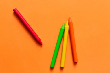 Turuncu arkaplanda renkli pastel boya kalemleri olan kümenin üst görünümü