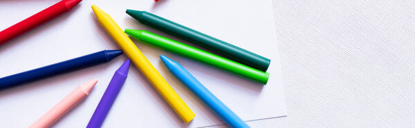 top view of colorful crayons on white paper and textured background, banner