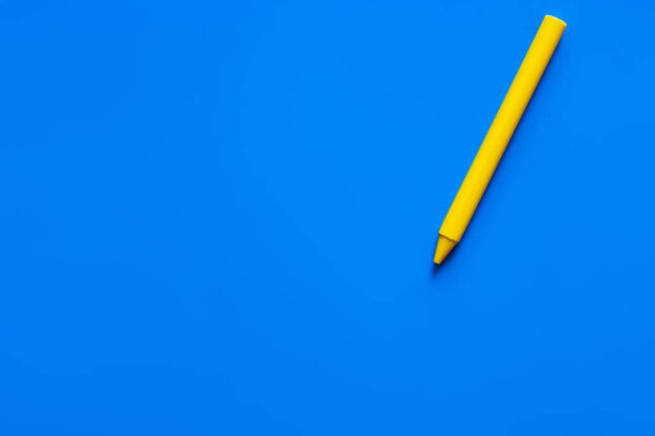 top view of yellow crayon on blue background 