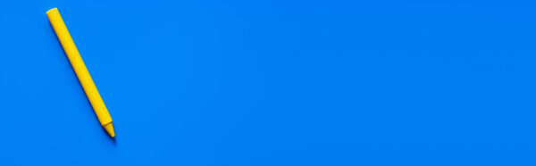 top view of yellow crayon on blue background, banner