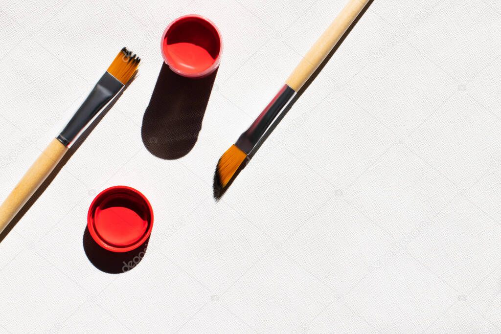 top view of paintbrushes near red paint on white textured background 