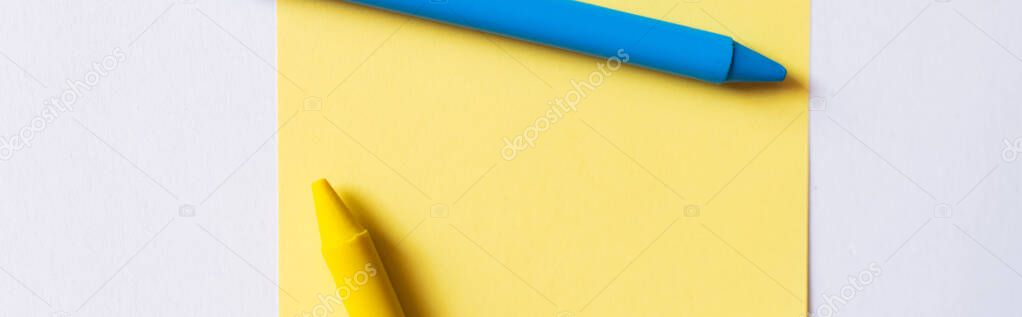 top view of blue and yellow crayons near paper note isolated on white, banner