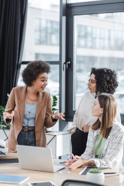 African american businesswoman talking to multiethnic colleagues near devices in office 