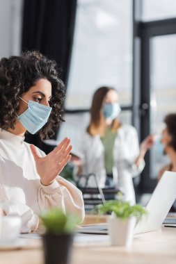 Tıp maskeli Müslüman iş kadını ofiste dizüstü bilgisayara bakıyor 