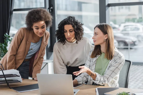 Mujer Negocios Señalando Computadora Portátil Cerca Colegas Multiétnicos Papeles Mesa — Foto de Stock