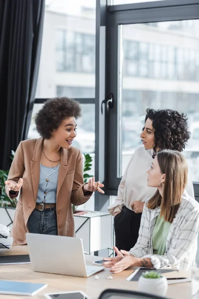 African american businesswoman talking to multiethnic colleagues near devices in office 