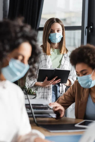 Businesswoman Medical Mask Holding Medical Mask Blurred Interracial Colleagues Working — Foto de Stock