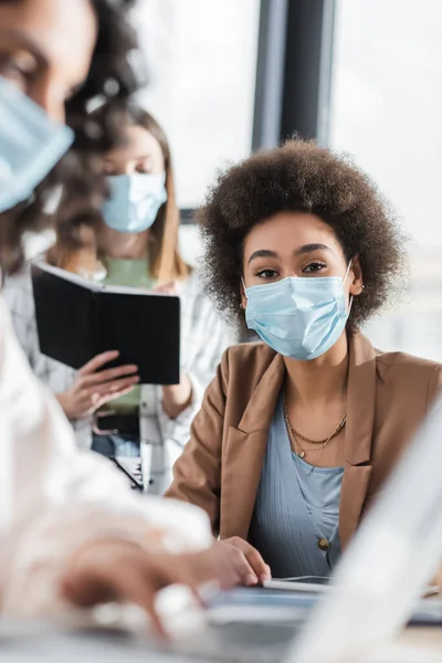 African American Businesswoman Medical Mask Looking Camera Blurred Interracial Colleagues — Foto Stock