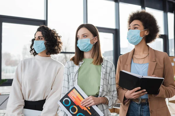 Jóvenes Empresarias Multiétnicas Con Máscaras Protectoras Sosteniendo Cuaderno Papel Con — Foto de Stock