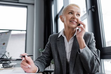 successful economist talking on mobile phone and smiling in office