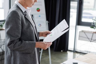 cropped view of financier standing with documents in office