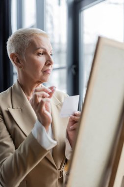 senior economist with short hair holding paper note near blurred flip chart