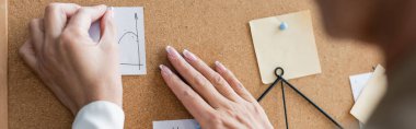 partial view of blurred banker pinning paper notes on corkboard, banner