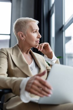 Düşünceli finansör bulanık laptopuyla oturuyor ve başka tarafa bakıyor.
