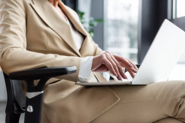 cropped view of sitting economist in formal wear typing on laptop