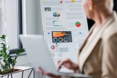 Önplanda bulanık dizüstü bilgisayarı olan kırpılmış bankacı yakınındaki grafik üzerinde seçici odak