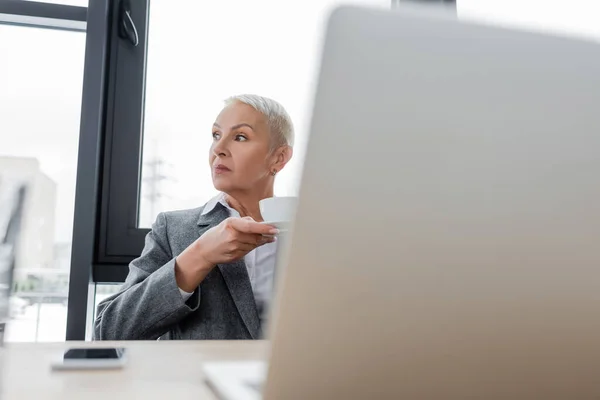 Thoughtful Businesswoman Coffee Cup Looking Away Blurred Laptop — 스톡 사진