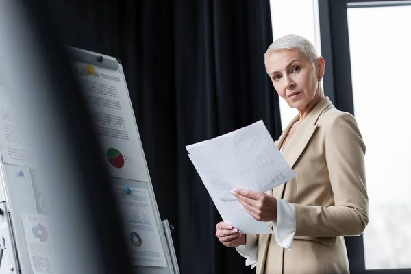 Senior Businesswoman Papíry Při Pohledu Kamery Blízkosti Flip Chart Infografikou — Stock fotografie