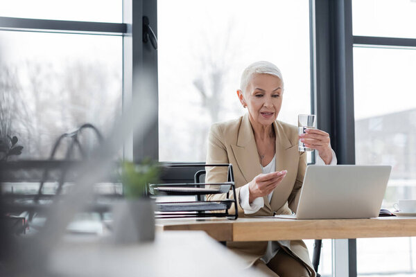 economist with glass of water talking near laptop during online conference