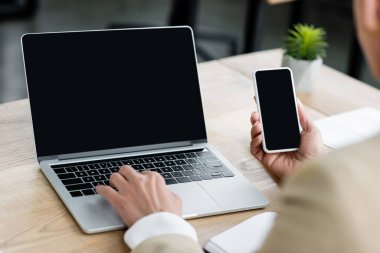 Bilgisayarda yazma ve boş ekran ile akıllı telefon tutma ekonomistin kırpılmış görünümü