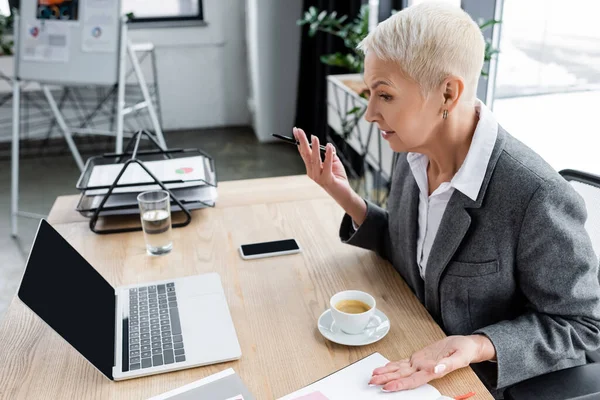 Senior Banker Gesturing Video Conference Laptop Coffee Cup Smartphone Blank — стоковое фото