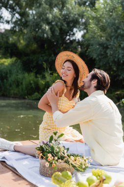 Romantik çift göl kenarında piknik yaparken gülümsüyor.