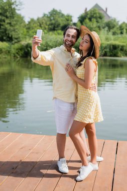 Mutlu genç çiftler göl kenarında selfie çekiyorlar.