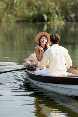 Hasır şapkalı mutlu kadın tekne turu sırasında romantik erkek arkadaşına bakıyor.